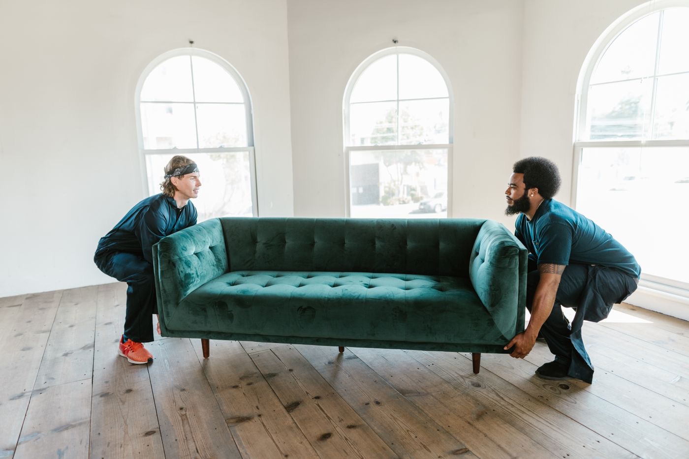 Two men carrying a green couch across a sunlit room